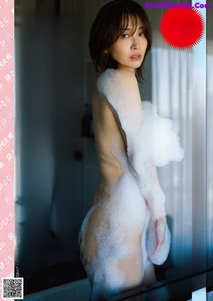 A naked woman is covered in foam in a bathroom.