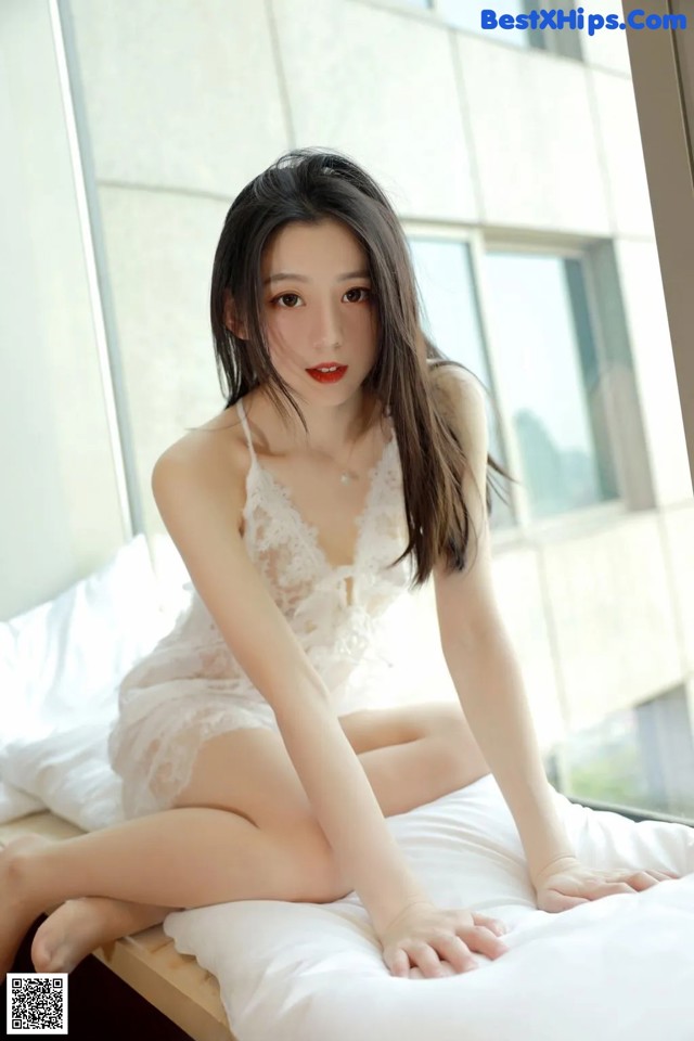 A woman in a white lingerie sitting on a bed.