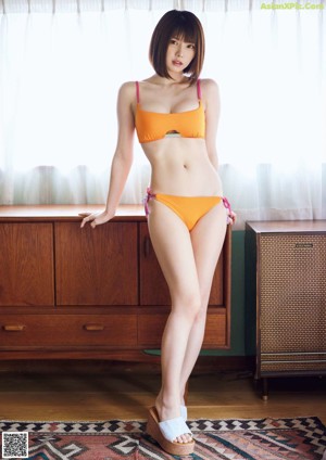 A woman in a pink and green bikini posing by a window.