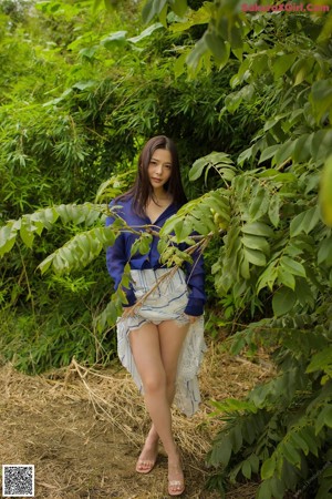 A woman in a blue shirt and white skirt crouching in the grass.