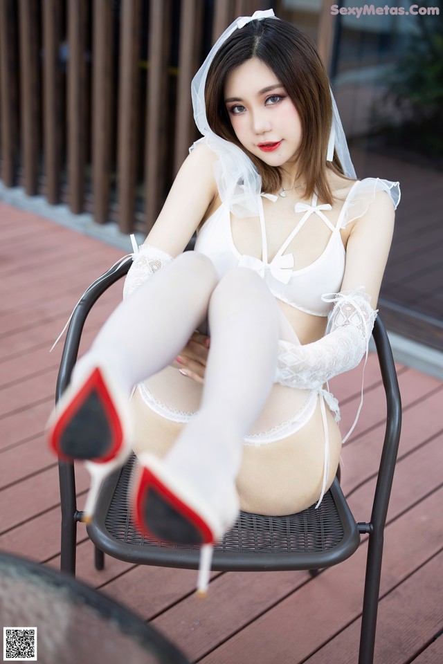 A woman in a white lingerie sitting on a chair.