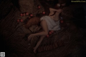 A nude woman sitting on a pile of hay next to apples.