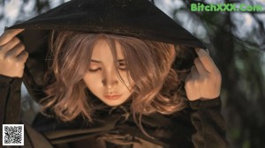 A woman sitting in front of a fire in the woods.