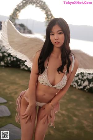 A woman in a bikini with angel wings standing in a field of flowers.