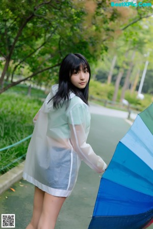 A woman in a clear raincoat holding a bunch of umbrellas.