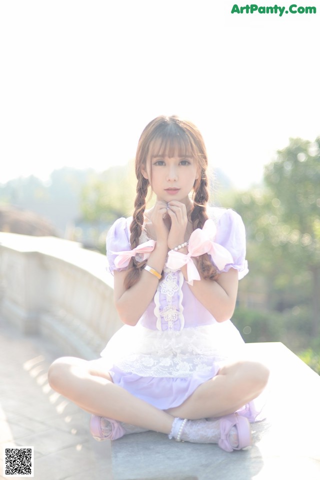 A young woman in a purple dress sitting on a ledge.